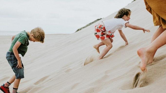 Three children clamber up a steep sand dune, which takes a lot of effort as the soft sand gives way under their little feet and hands